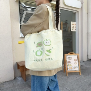 Detail of cute bear and apple embroidery on a yellow canvas tote bag with shoulder strap