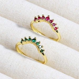 Close-up of gold crown rings with red and green gemstones on beige textured fabric