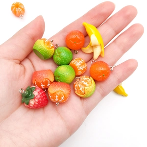 Hand holding various acrylic fruit charms including strawberry and orange with metal rings