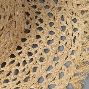 Detailed macro view of hollow weave patterns and frayed edges on natural raffia sun hat