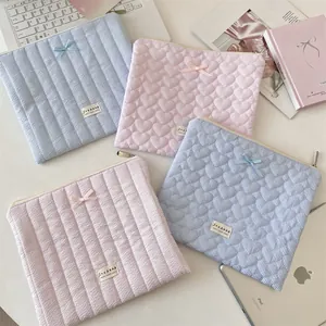 Close-up of quilted laptop sleeves with ribbon bows and heart patterns on soft cotton fabric