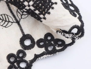 Macro shot of ethnic black embroidery and hollow-out lace on cream cotton-linen fabric
