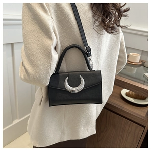 Détail d'un sac bandoulière en cuir noir avec boucle argentée en croissant sur un modèle