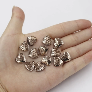 Macro detail of heart-shaped scales charms in champagne gold held in palm for size reference