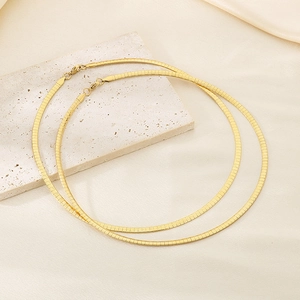 Detailed macro view of two gold flat snake bone necklaces on a textured stone surface