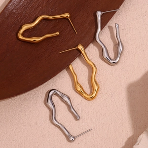 Flat lay of polished 18K gold and silver wave-shaped V earrings on a textured background