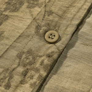 Macro detail of khaki jacquard shirt fabric with floral embroidery and matte buttons