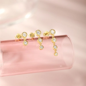 Macro shot of three gold S925 silver stud earrings with white zircons on pink glass