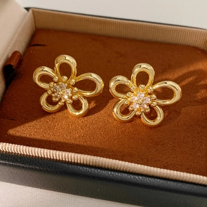 Detail of gold hollow flower earrings with sparkling cubic zirconia centers on brown velvet