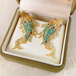 Detailed close-up of fish-shaped earrings with blue and red crystals in green velvet box