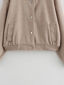 Detailed close-up of camel tweed jacket with silver metal snaps and ribbed hem texture