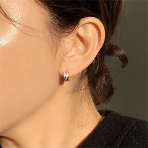 Close-up of a model wearing tiered striped sterling silver hoop earrings with a metallic finish