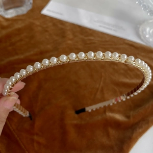 Close-up of elegant gold metal headband with white faux pearl embellishments and black tips