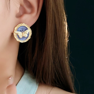 Close-up of vintage round gold earrings with blue enamel and relief butterfly motif