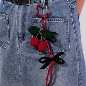 Handmade woven cherry keychain with heart carabiner and black bow on denim fabric