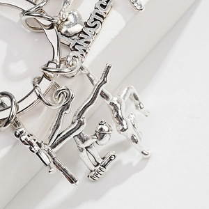 Silver gymnastic themed metal keychain with heart tag and athlete charms on white background