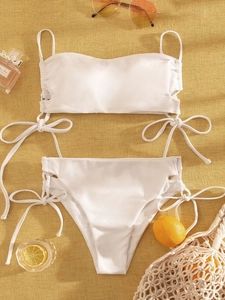Flat lay of a white two-piece bikini with drawstring side ties on a yellow fabric background