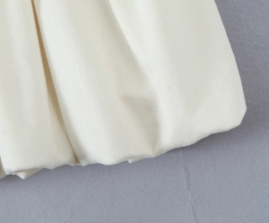 Detailaufnahme des plissierten cremefarbenen Stoffes an einem schicken Polo-Minikleid