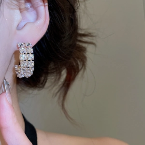 Close-up of gold C-shaped hoop earrings featuring multi-row inlaid square cubic zirconia