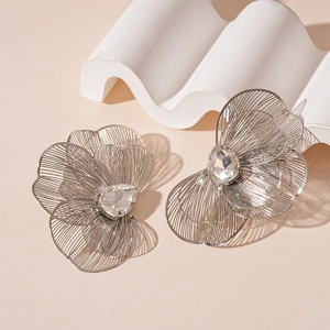 Detailed macro view of silver hollow floral earrings with crystal center and petal layers