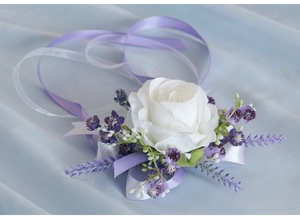 Detail of white rose wrist corsage with purple berries and satin ribbons on blue fabric