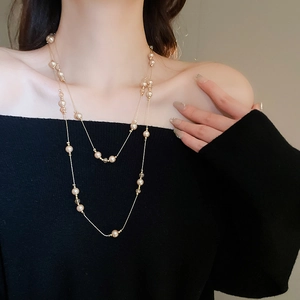 Collier double rang doré avec perles champagne et cristaux sur un pull noir chic