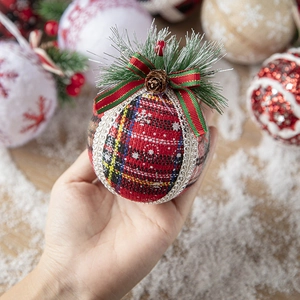 Plaid Christmas ball ornament with pine needles and pinecone on a warm festive background