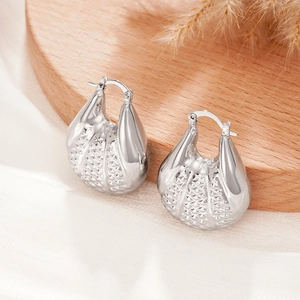 Détail de boucles d'oreilles argentées avec texture en losanges sur un tissu soyeux