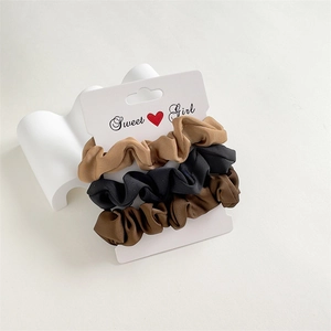 Détail de trois chouchous en satin de couleurs kaki, noir et marron sur carte de support