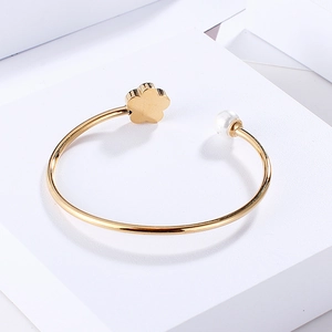 Detail of gold open bangle featuring a floral motif and a white pearl on a white pedestal