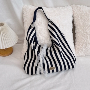 Vue détaillée du sac en toile rayé avec bordure en dentelle et logo en métal sur lit