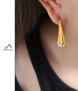 Detail of a gold stainless steel water-drop earring with white resin inlay on a model