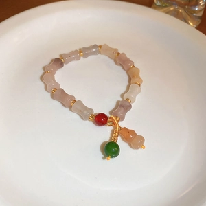 Macro detail of agate bead bracelet with bamboo shapes and gourd charm on white plate
