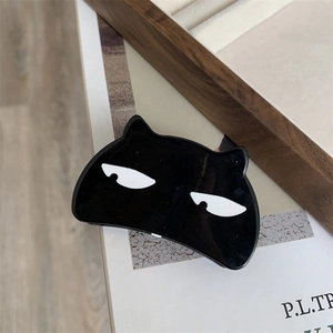 Detail view of a black cat-shaped acetate hair claw with white eyes on a white surface