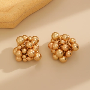 Close-up of golden cluster beaded earrings with polished spheres on beige background