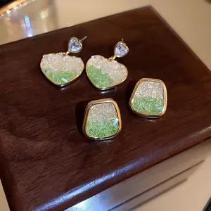 Detailed macro of gold-plated heart and square earrings with green gradient crystal inlay