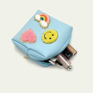 Detail of blue leather makeup bag with chenille patches and gold zipper closure