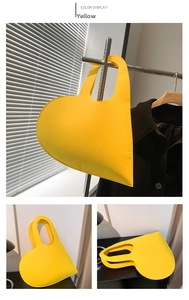 Detail view of a bright yellow heart-shaped felt handbag with a sleek cut-out handle