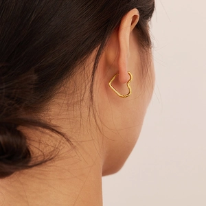 Detail view of a model wearing a gold heart-shaped earring in polished stainless steel