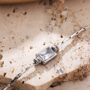 Silver woven chain necklace with rectangular clear zircon pendant on beige stone background