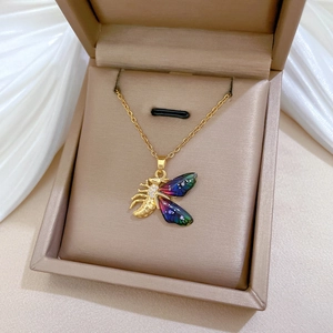 Detailed shot of a gold bee necklace with rainbow enamel wings in a beige jewelry box