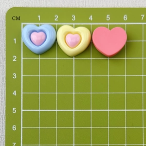 Detailed view of colorful 2cm resin heart charms on a green centimeter scale mat