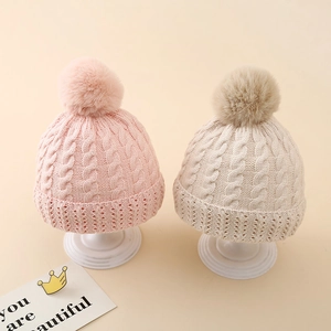 Detail of cable knit baby hats with pom-poms in pink and beige on white stands