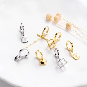 Minimalist gold and silver geometric heart and cube drop earrings on a ceramic plate