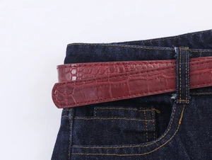 Détail d'une ceinture rouge texture crocodile sur un jean en denim bleu foncé