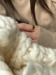 Close-up of a gold ring with a green oval gemstone on a hand over a beige knit