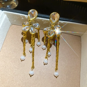 Detailed view of floral stud earrings with gold tassels and white pearl accents