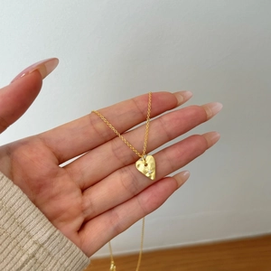 Detailed close-up of a golden heart pendant necklace with a small zircon stone inlay