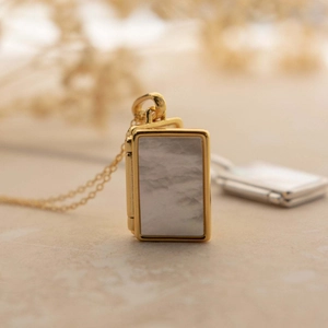 Close-up of golden book-shaped locket pendant with white marble inlay on a delicate chain