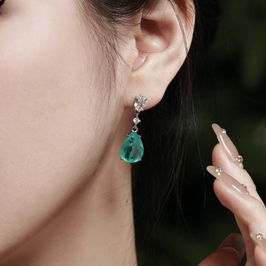 Close-up of emerald green pear-shaped drop earring on model with sparkling accents
